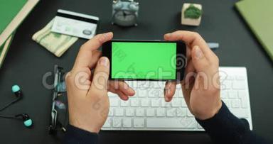 男人拿着一个绿色屏幕的黑色智能手机在工作桌上滚动一些东西