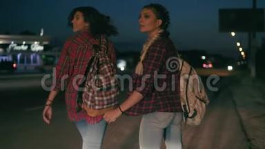 两个年轻的女搭便车者站在一旁，手里拿着背包，要求在晚上阻止过往的汽车