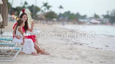 一家人的妈妈和孩子享受白色海滩上的海景。 一家人放松地坐在日光浴床上看着美丽
