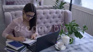 在网上学习，漂亮的女孩用钢笔在笔记本上写笔记，坐在桌子上，拿着笔记本在咖啡馆里