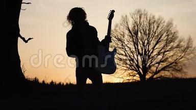 日落时分，人们在靠近树的田野里弹电吉他，唱抒情歌曲。 剪影
