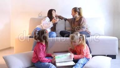 两个女孩坐在地板上翻书，年轻妈妈坐在沙发旁边讨论问题。