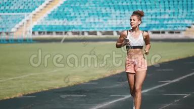 一个穿着运动服的强壮女孩在体育场奔跑的肖像。 美丽的女孩在体育场奔跑，倾听