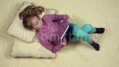 有趣的<strong>小女孩躺在沙发上</strong>看书。 顶部视图