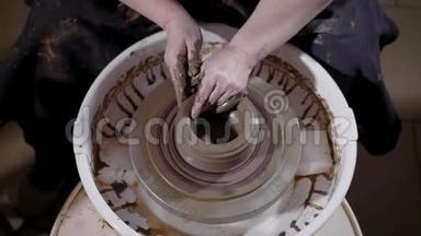 熟练的工匠坐在陶艺创作车间，俯视图，正在塑造和校正车轮头上的泥杯