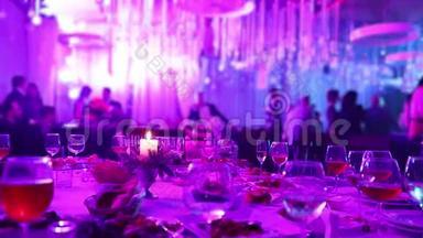 有眼镜和蜡烛的餐厅的宴会桌。 人们在桌子的背景下跳舞。 宴会桌桌
