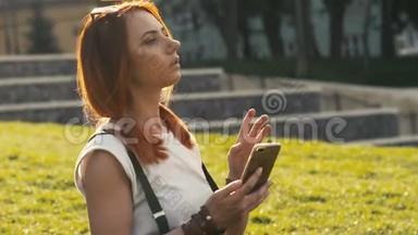 戴着红色头发的女人拿着手机在夏季公园