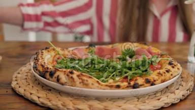 披萨店的厨师准备一个披萨，并用意大利火腿装饰它。 绿色草本植物接近