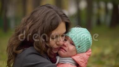 一幅美丽的年轻女子和一个<strong>哭</strong>泣的孩子在秋天公园的肖像。 小女孩在<strong>哭</strong>。 年轻的母亲安慰她