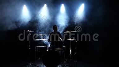 精力充沛的音乐家在鼓上演奏好音乐。 黑色烟熏背景。 背光。 剪影。