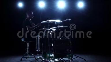 鼓手在鼓上大力演奏旋律。 黑色背景。 背光。 剪影。 慢动作