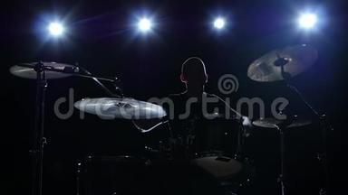 鼓手在鼓上大力演奏旋律。 黑色背景。 背光。 剪影。 慢动作