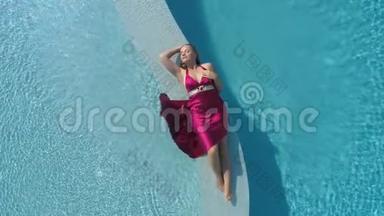 年轻的金发女郎穿着红裙子躺在游泳池里