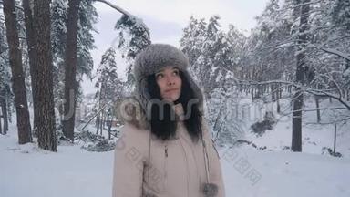 戴帽子的年轻女子正在冬天的森林里散步。 公园冬天一个女孩的肖像。