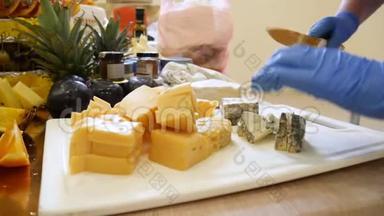戴着蓝色橡胶手套的人手中锋利的刀把奶酪切成碎片放在白色托盘上特写