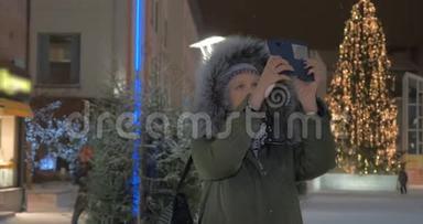 女人在街上用圣诞节的光照拍手机