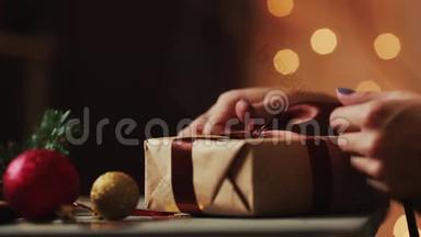 在圣诞灯光的背景下，女人`手把丝带绑在牛皮纸上。 背景