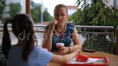 母亲和女儿正坐在一张桌子旁的一家街头<strong>咖啡</strong>馆里。 喝<strong>咖啡奶昔</strong>，吃薯条。