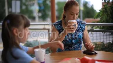 母亲和女儿正坐在一张桌子旁的一家街头<strong>咖啡</strong>馆里。 喝<strong>咖啡奶昔</strong>，吃薯条。