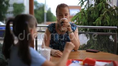 母亲和女儿正坐在一张桌子旁的一家街头咖啡馆里。 喝咖啡奶昔，吃薯条。