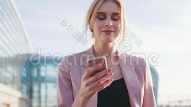 可爱的金发女人穿着粉红色时尚的服装经过机场，使用她的手机，玩味地环顾四周。 衬裙