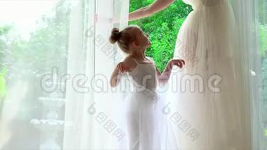 小芭蕾舞女将在老师后面重复。 两个芭蕾舞演员在大窗户旁边，有白色的窗帘。 美丽美丽