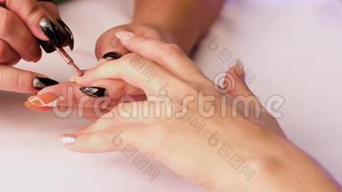 美甲师用棕色的清漆把女人的指甲盖在左<strong>手中</strong>指上。