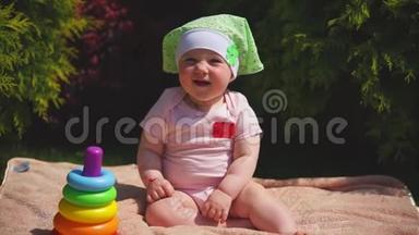 一个快乐的新生儿坐在公园的毛巾上，<strong>接下来</strong>是一个玩具金字塔
