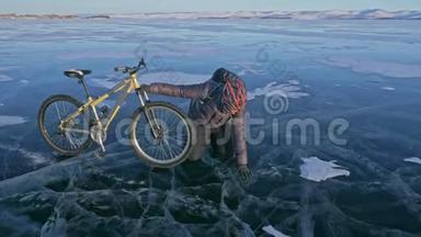 人和他的自行车在冰上。 他看着裂缝里美丽的冰.. 骑自行车的人穿着灰色羽绒服