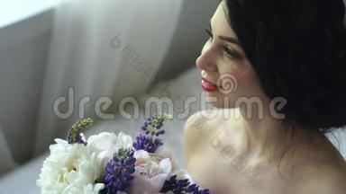 一个温柔迷人的黑发女人的早晨。 美丽的新娘微笑着，<strong>看</strong>着<strong>窗外</strong>和一束花