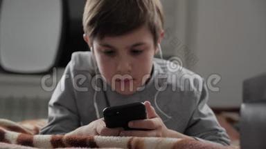小孩玩手机带耳机在家。 小孩躺在床上使用智能手机