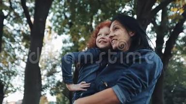 一位美丽的妈妈和她可爱的女儿正在秋天的公园里散步。 妈妈把女儿抱在怀里。 他们