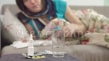 桌子，椅子上的喷雾和水，年轻的生病的女人在背景上为喉咙吃药。