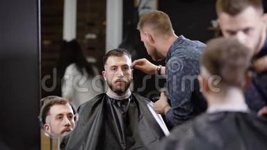 时尚的理发师正在刮太阳穴，理发店里坐在扶手椅上看着一个留胡子的人的理发器