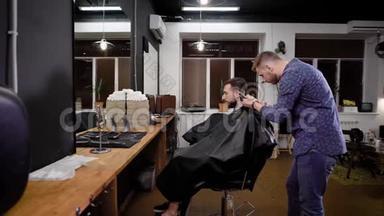年轻的理发师在扶手椅上走来走去，在理发店里和剪刀一起理发。 有胡子的男人坐在