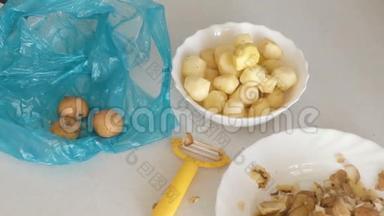 盘子里的小土豆，厨房桌子上的果皮和剥皮机。 塑料蓝色袋子上的未剥皮土豆。