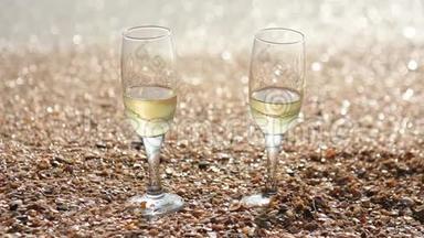 两杯香槟站在沙滩上，海边有<strong>小贝壳</strong>，背景中海浪冲刷着海岸