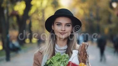 年轻漂亮的女人穿着时髦的外套在公园里散步，手里拿着<strong>一包</strong>产品，微笑着看着。