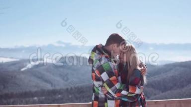 年轻男子温柔地拥抱他迷人的金发女朋友，同时站在山上的观景台上。 令人惊叹