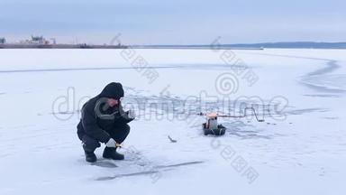 穿着深色衣服的老渔夫在<strong>冰冻</strong>的河上钓着冬天的<strong>鱼</strong>竿