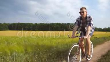 戴墨镜的人骑自行车沿着乡村小径户外。 年轻的微笑男子骑着老式自行车在<strong>农村公路</strong>