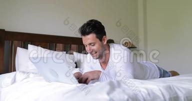 年轻人用笔记本电脑躺在床上快乐的微笑男人在床上聊天