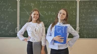 两个女学生在用数学公式画的学校董事会背景下摆姿势。