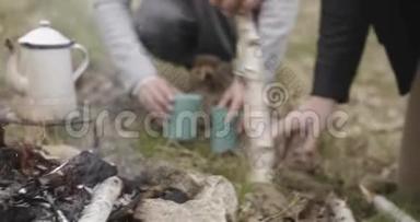 人在露营帐篷附近的火地上用木棍打木头。 而女人准备<strong>热饮料</strong>。 两个相爱的人
