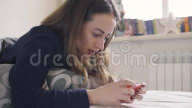 年轻女子在智能手机上玩游戏，躺在家里的床上