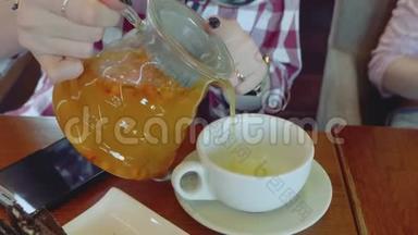 一个白人女人的手把沙棘茶从透明茶壶倒入白色的杯子里。 近距离观看