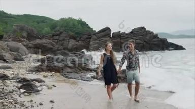 年轻夫妇女孩和男人沿着海滩散步，说话和牵手，前景。 美丽的海景和