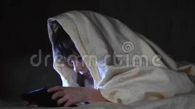 一个<strong>孩子</strong>晚上在毯子下面使用平板<strong>电脑</strong>。 这个男孩<strong>玩电脑</strong>游戏