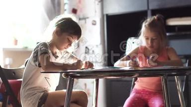 两个6岁和7岁的姐妹一<strong>起坐</strong>在桌子旁。 孩子们在阳光下用蜡笔画画