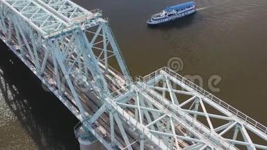 从空中俯瞰铁路大桥，上面有一列移动的火车，穿过流经一个主要城市的河流